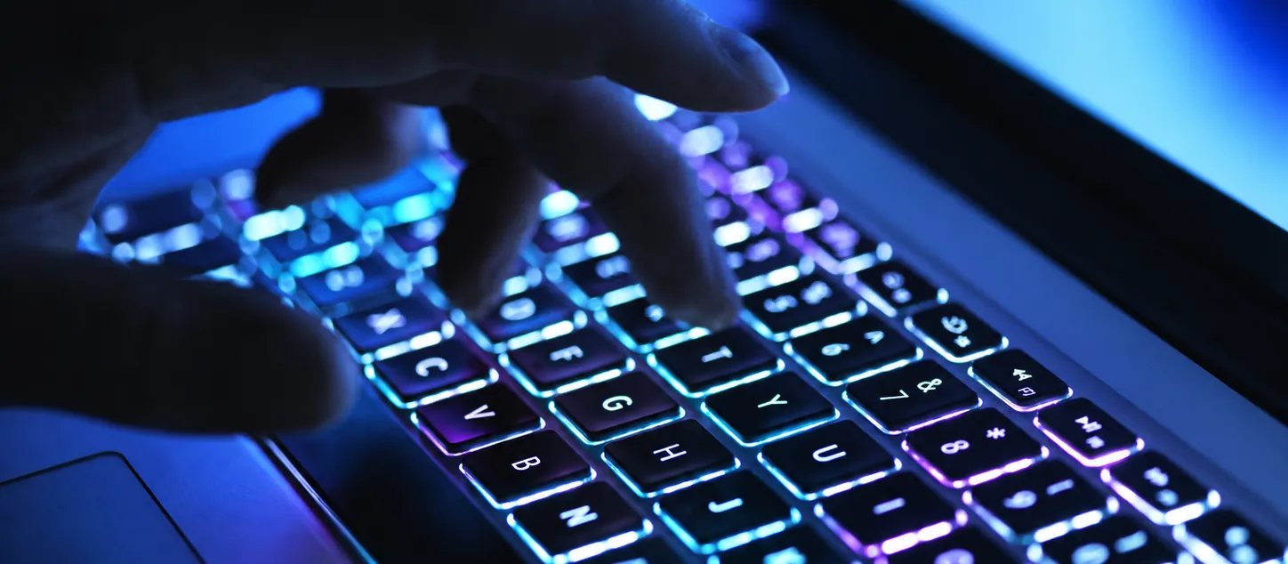 Hand op een verlicht toetsenbord in het donker, symbool voor het PHP-lek en hackers